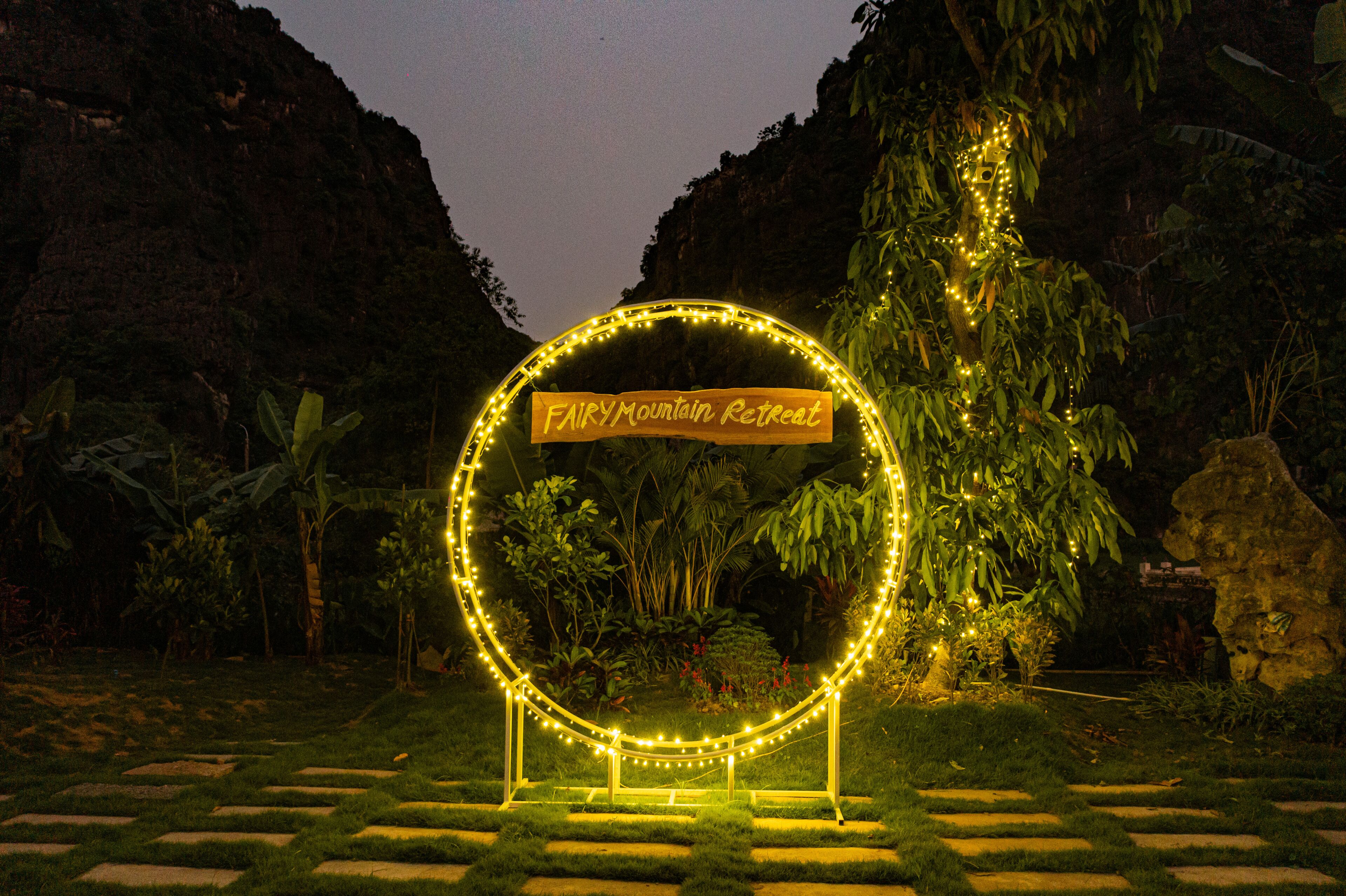 A sign for the Fairy Mountain Retreat surrounded by lush greenery and stone pathways.