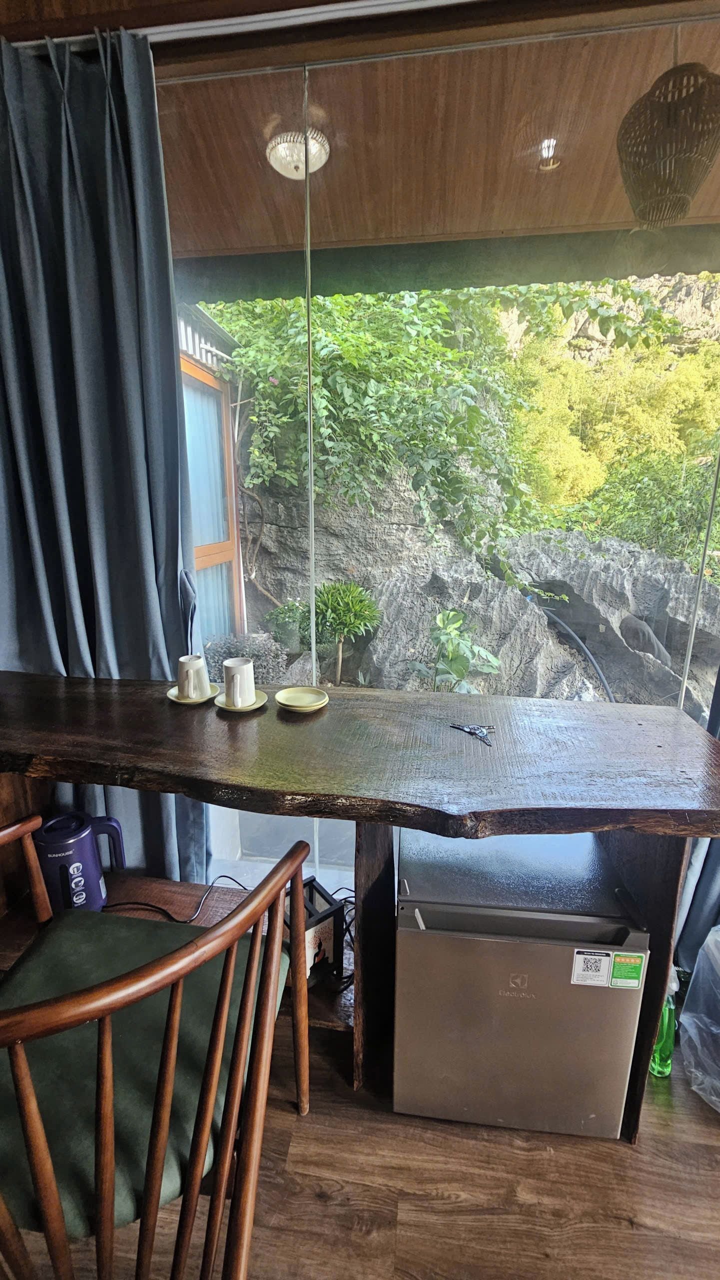 A wooden table with a view of a rocky landscape through a window, a chair, and a small refrigerator.