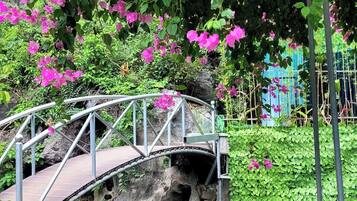 A stone bridge over a stream with pink flowers and greenery.