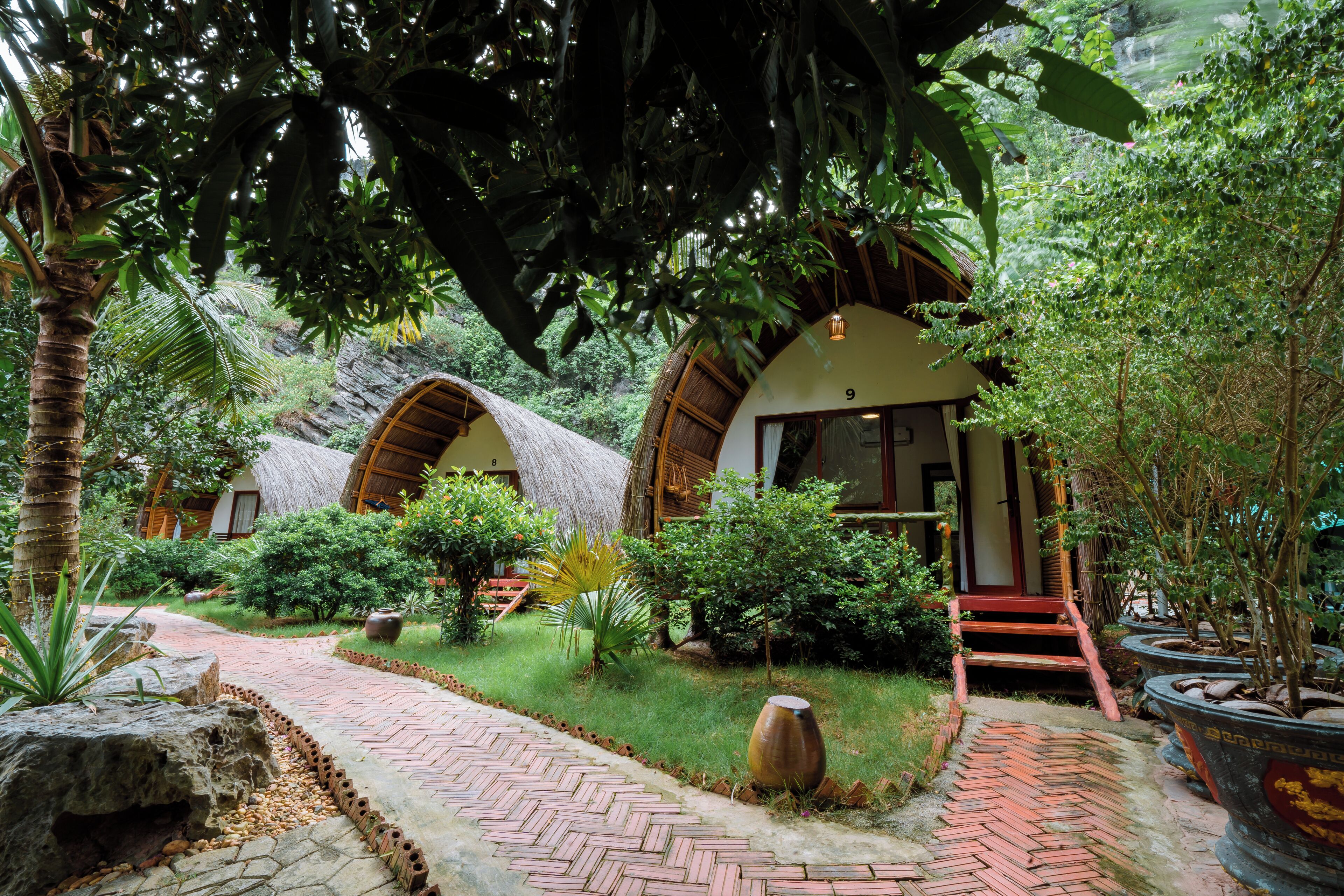 Un complexe hôtelier tropical doté de bungalows aux toits de chaume, d’un sentier dallé et d’une végétation luxuriante.