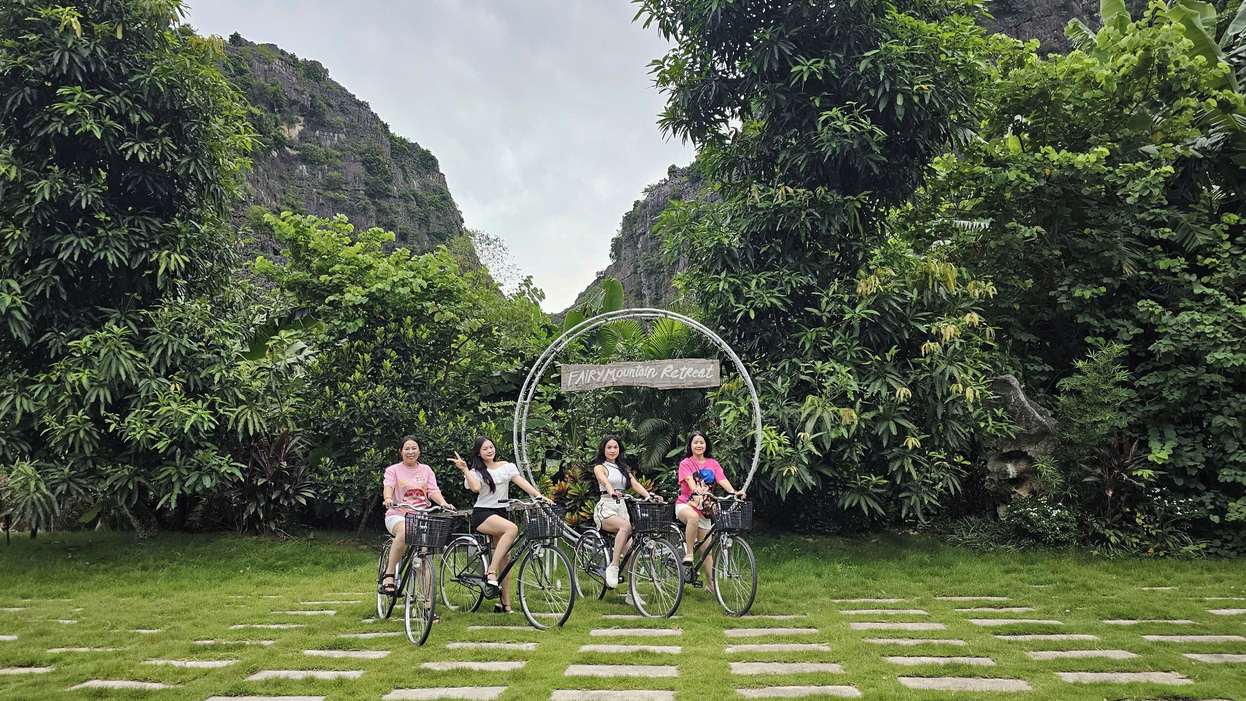 Un grupo de personas en bicicleta en un entorno natural exuberante y verde, con un letrero que dice 'Fairy Mountain Retreat'.