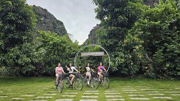 Un grupo de personas en bicicleta en un entorno natural exuberante y verde, con un letrero que dice 'Fairy Mountain Retreat'.