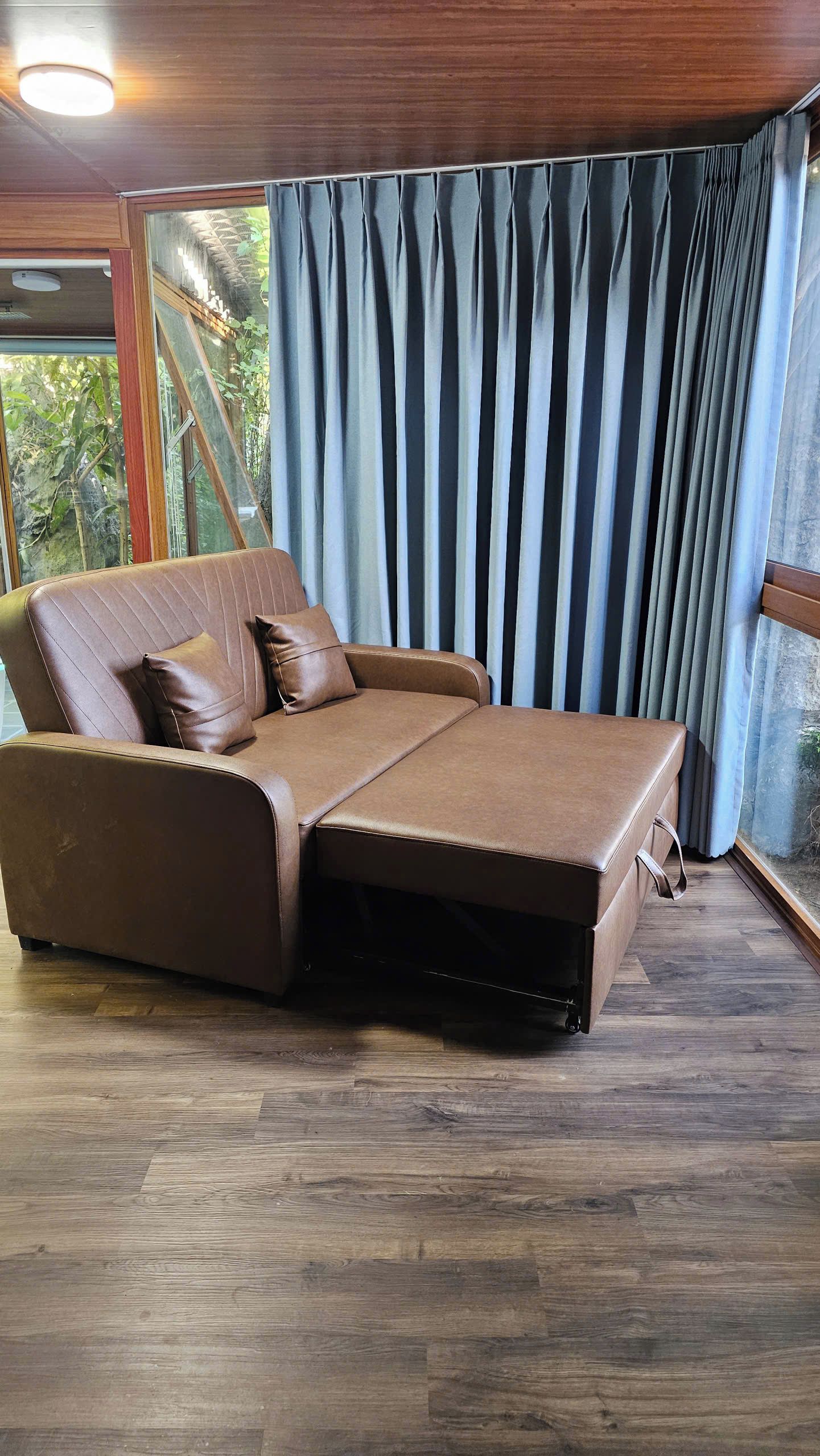 Ein Zimmer mit einem braunen Ledersofa, Holzboden und einem Fenster mit blauen Vorhängen.