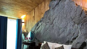 A bedroom with a bed, a dresser, a mirror, and a large rock wall.