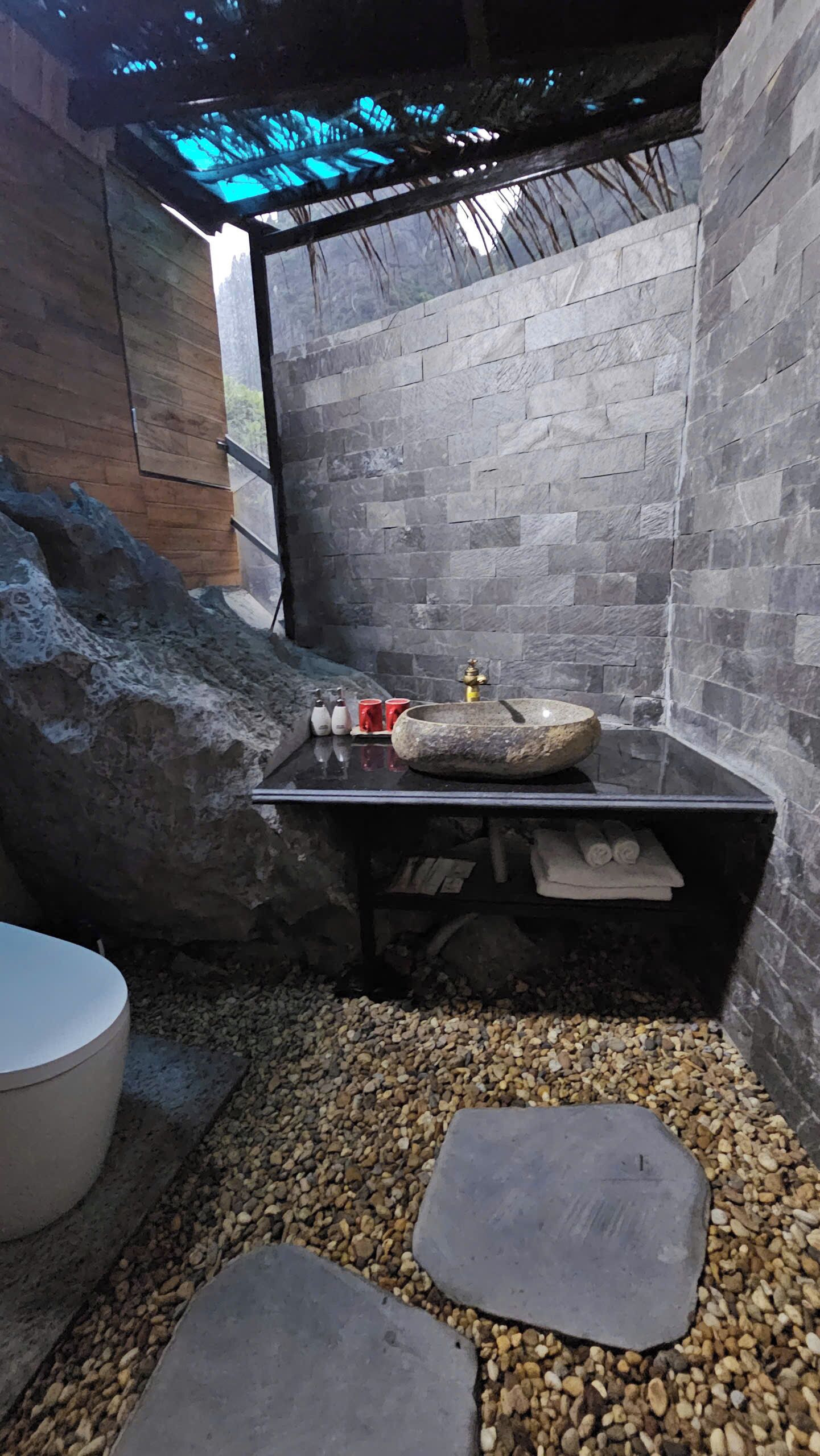 A bathroom with a stone sink, a wooden door, and a pebble floor.