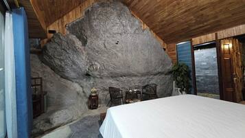 Une pièce dotée d’un grand mur en pierre, d’un plafond en bois et d’un lit recouvert d’une couverture blanche.
