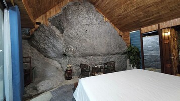 Une pièce dotée d’un grand mur en pierre, d’un plafond en bois et d’un lit recouvert d’une couverture blanche.