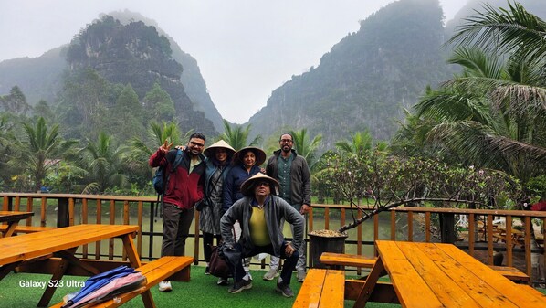 A group of people posing on a wooden deck with a view of a mountainous landscape and palm trees. - Fairy Mountain Retreat (Ninh Binh)