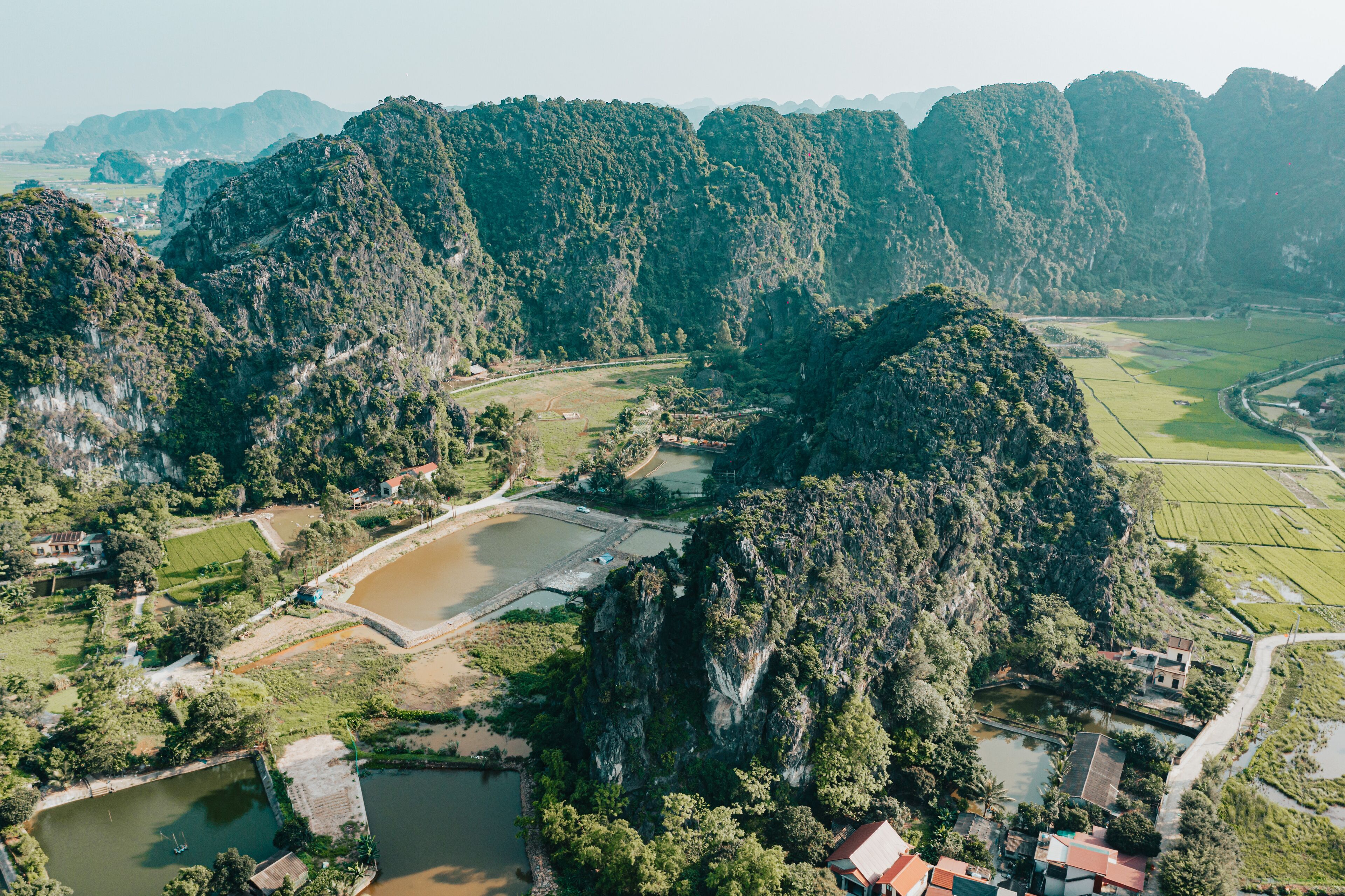 An aerial view of a mountainous area with terraced fields, a small body of water, and a few buildings.