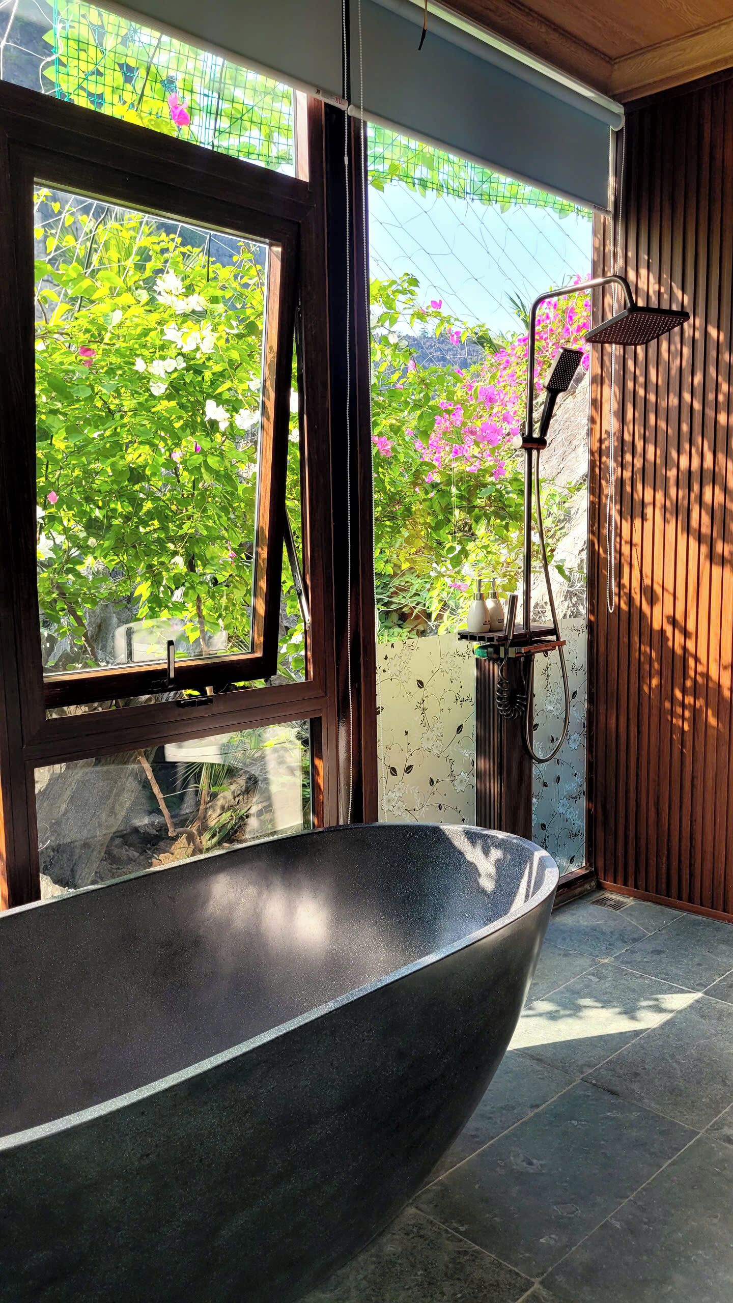 Un bagno moderno con una vasca da bagno freestanding, una finestra con vista sul verde e un angolo doccia con soffione a pioggia.