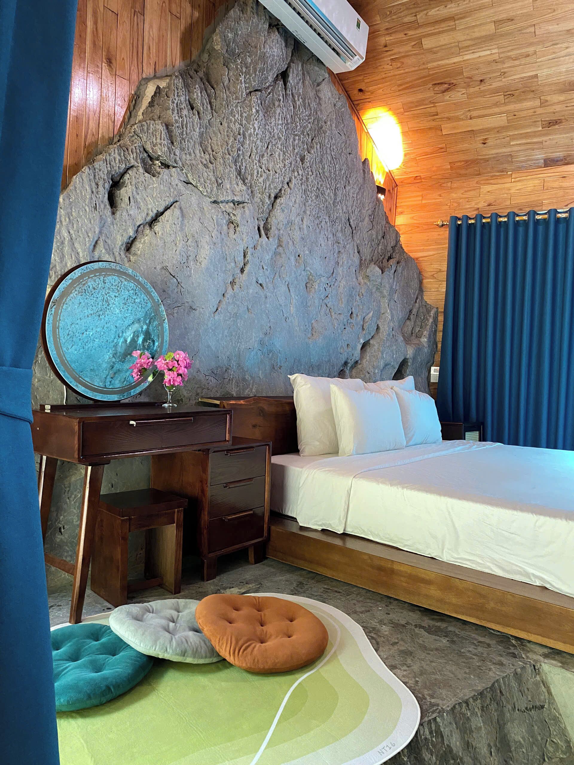 Ein Schlafzimmer mit einer großen Felswand, einem Bett, einem Schreibtisch mit Schubladen, einem Spiegel und einem kleinen Tisch mit Blumen.