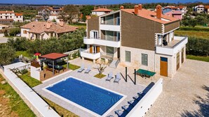 A modern two-story house with a swimming pool, outdoor seating, and a view of the surrounding neighborhood.