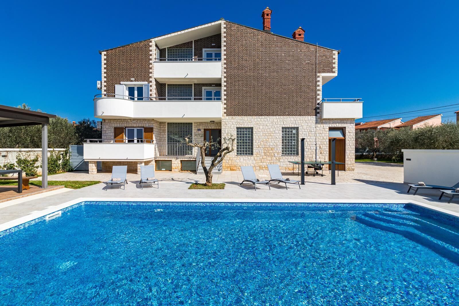 Une maison à deux étages avec une piscine, un espace salon extérieur et un petit jardin.