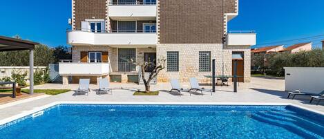 Une maison à deux étages avec une piscine, un espace salon extérieur et un petit jardin.