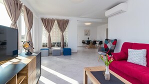 A modern living room with a TV, seating, and a dining area in the background.