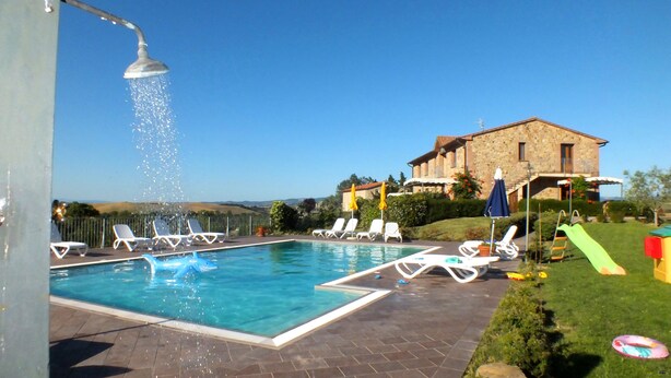 A swimming pool with a shark float, lounge chairs, and a stone building in the background. - Apartment in Farmhouse in Lajatico with 3 bedrooms and 3 bathrooms (Orciatico)
