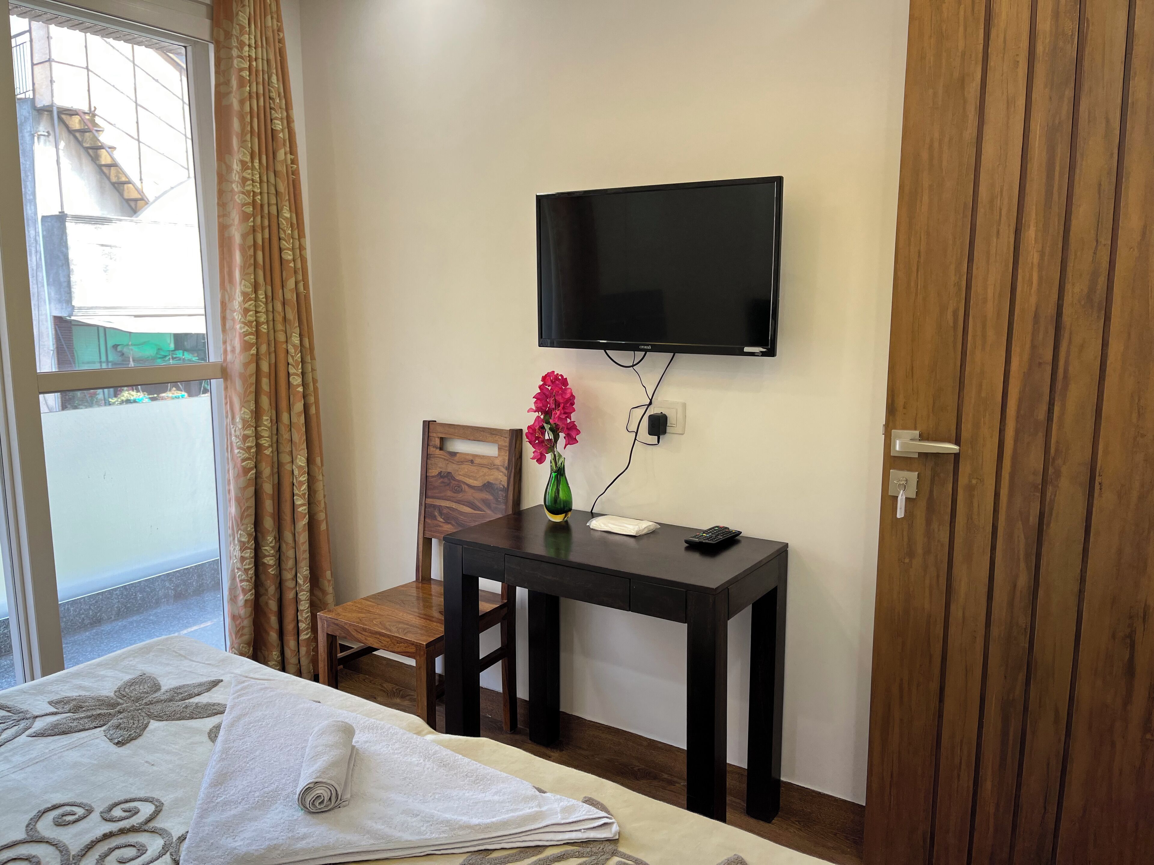 Une chambre d’hôtel avec un lit, un bureau et une chaise, une télévision et une fenêtre avec des rideaux.