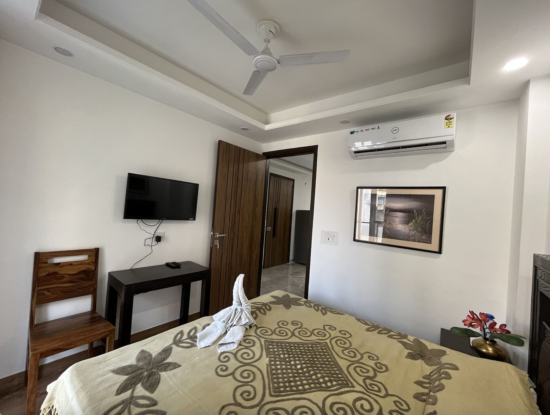 Una habitación de hotel con cama, televisión, aire acondicionado, una silla de madera y un escritorio.