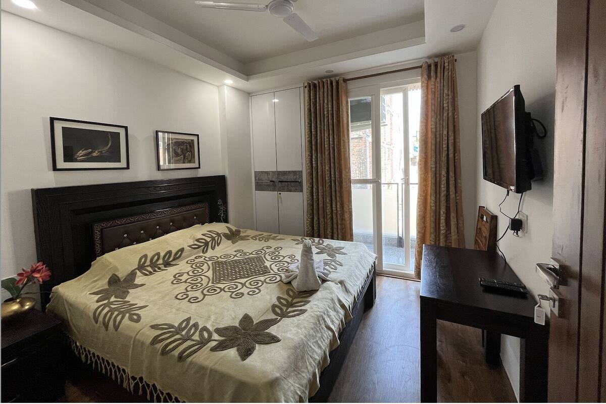 A bedroom with a bed, a desk, a television, and a ceiling fan.