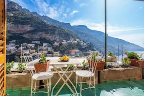 A terrace with a table and chairs, overlooking a coastal village with buildings on a hillside. - Rosa House - Breathtaking View of the Amalfi Coast (Positano)