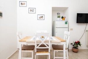 A dining area with a white table, four chairs, and a refrigerator in the background. - Rosa House – Private Terrace with Spectacular Views in the Heart of Positano (Positano)