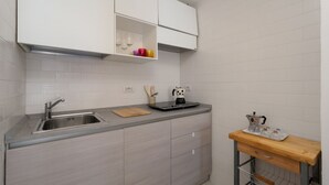 A kitchen with a sink, countertop, cabinets, and a small wooden table with a coffee maker. - Rosa House - Breathtaking View of the Amalfi Coast (Positano)