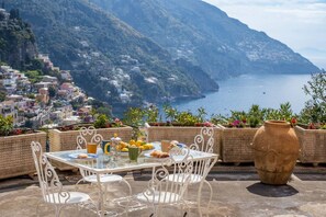 A table with chairs and a vase, overlooking a coastal town with buildings and a sea view. - Rosa House - Breathtaking View of the Amalfi Coast (Positano)