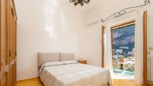 Een slaapkamer met een bed, nachtkastje, raam met uitzicht en een deur naar buiten.