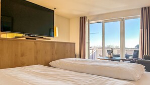 A hotel room with two beds, a TV, and a balcony with a view.