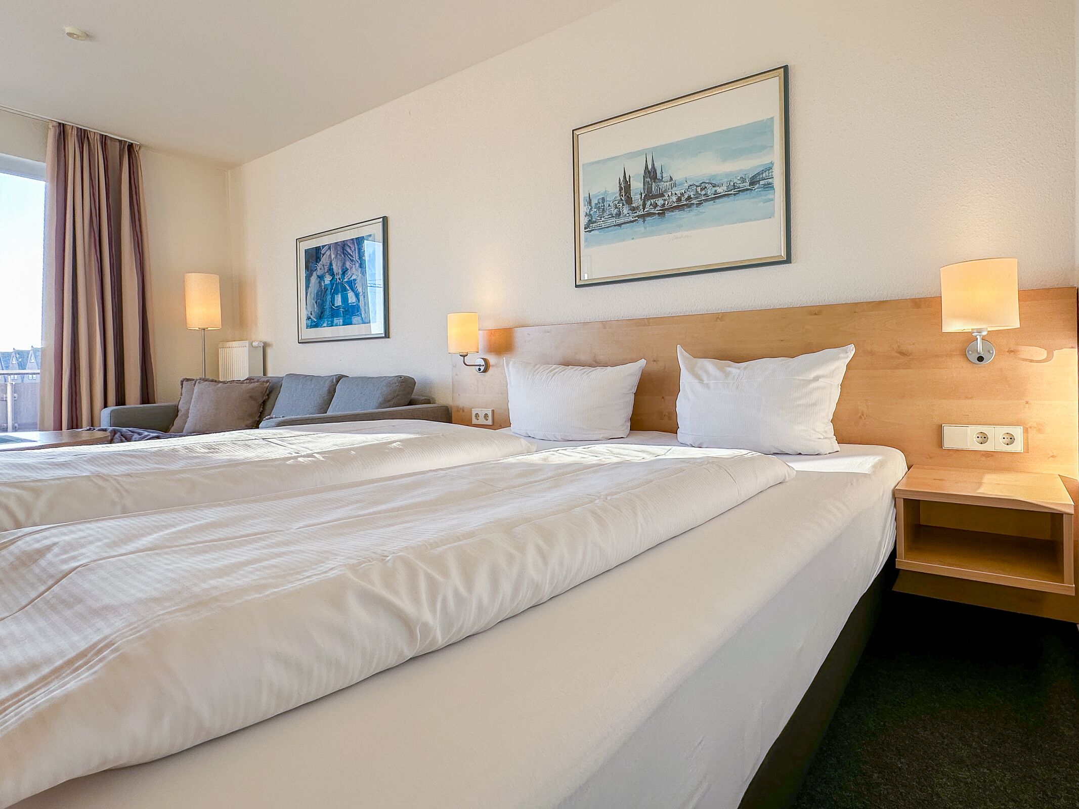 A hotel room with two beds, a sofa, and a view of a cityscape.
