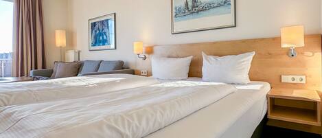 A hotel room with two beds, a sofa, and a view of a cityscape.