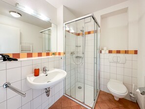A bathroom with a glass-enclosed shower, a sink with a mirror above it, and a toilet. - Appartement Sinnewyn (Westerland)