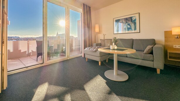 A hotel room with a balcony, a sofa, a small table, and a painting on the wall.