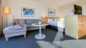 A hotel room with a sofa, a bed, a desk, and a dresser. There are two paintings on the wall.