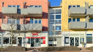 A multi-story residential building with balconies, a visible storefront with signage, and a clear blue sky.