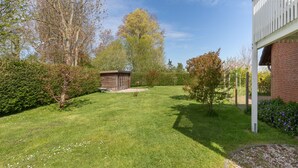 A well-maintained lawn with a wooden structure, surrounded by trees and a brick building.