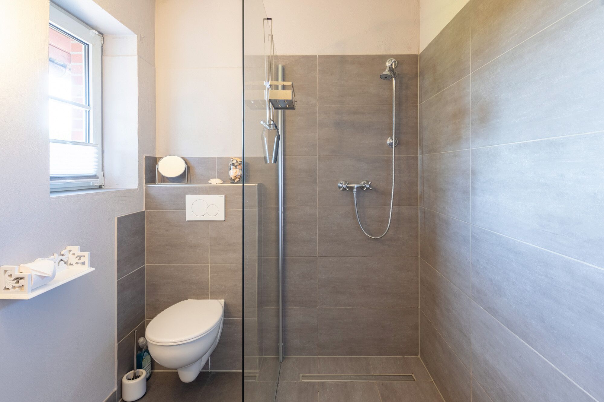 Une salle de bain moderne avec une douche à parois de verre, des toilettes et une petite étagère contenant des articles de toilette.