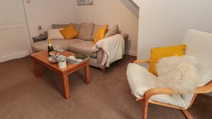 Un salon chaleureux avec un canapé, un fauteuil et une table basse. Un tableau encadré est accroché au mur et une décoration en forme d’étoile orne le plafond.