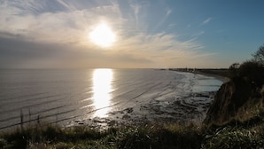 Un paysage côtier avec une plage, un ciel dégagé et le soleil se reflétant sur l’eau.