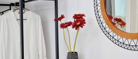 A white shirt hanging on a rack, a vase with red flowers, and a mirror with a geometric frame.