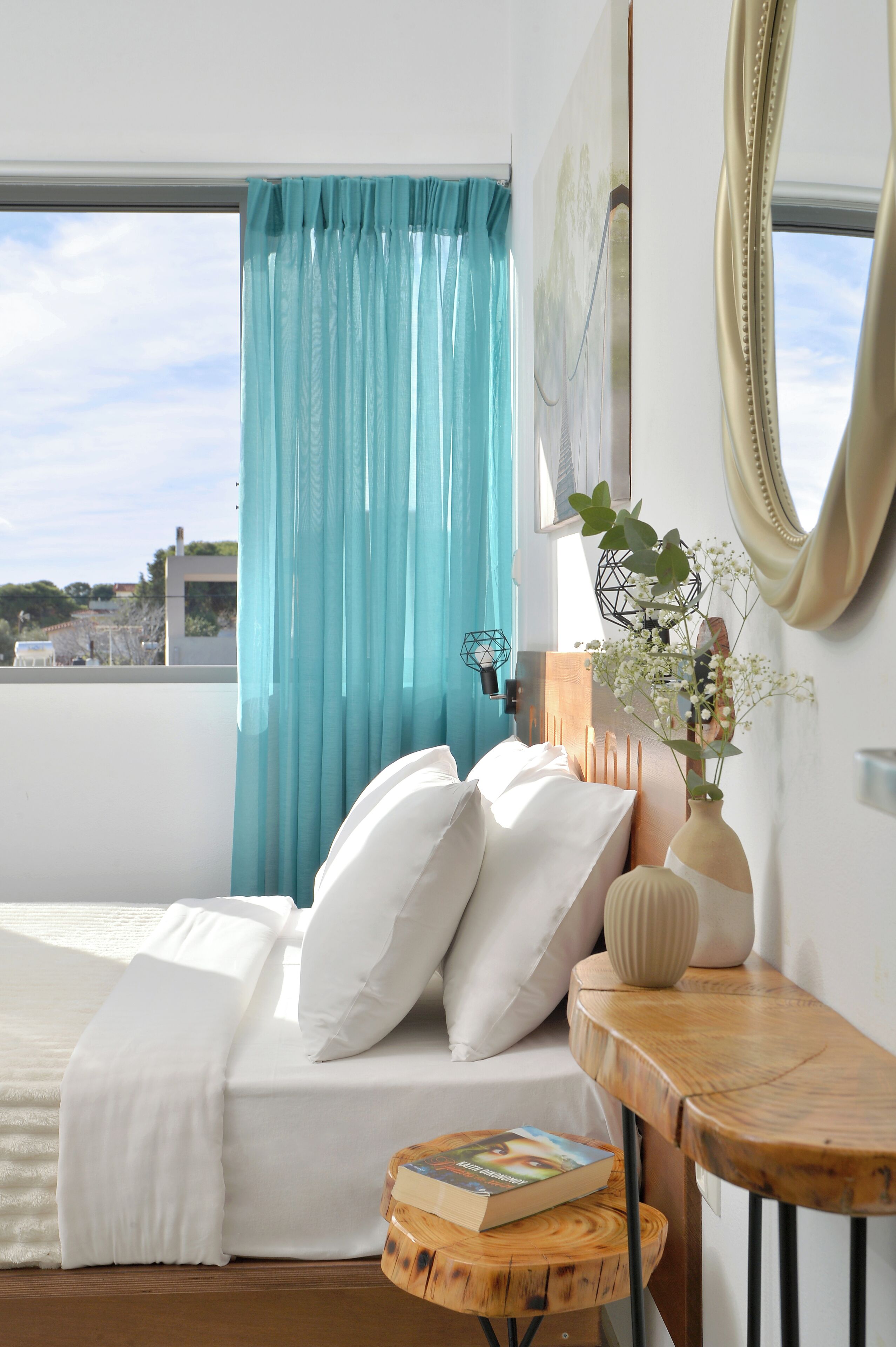 A bedroom with a bed, a bedside table, a window with curtains, and a view of the outside.