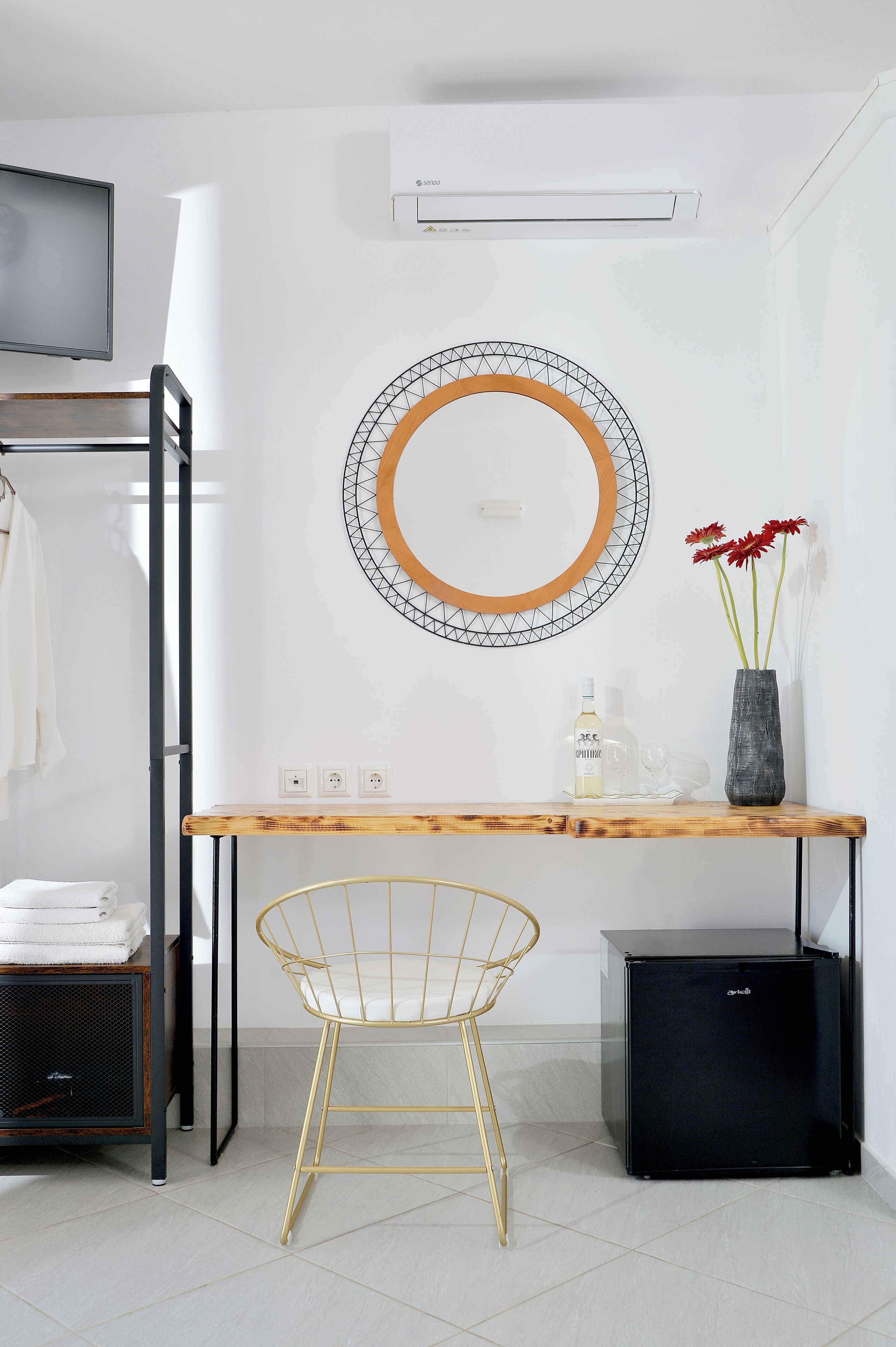 A modern room with a wooden desk, a gold chair, a black mini-fridge, and a mirror with a geometric frame.