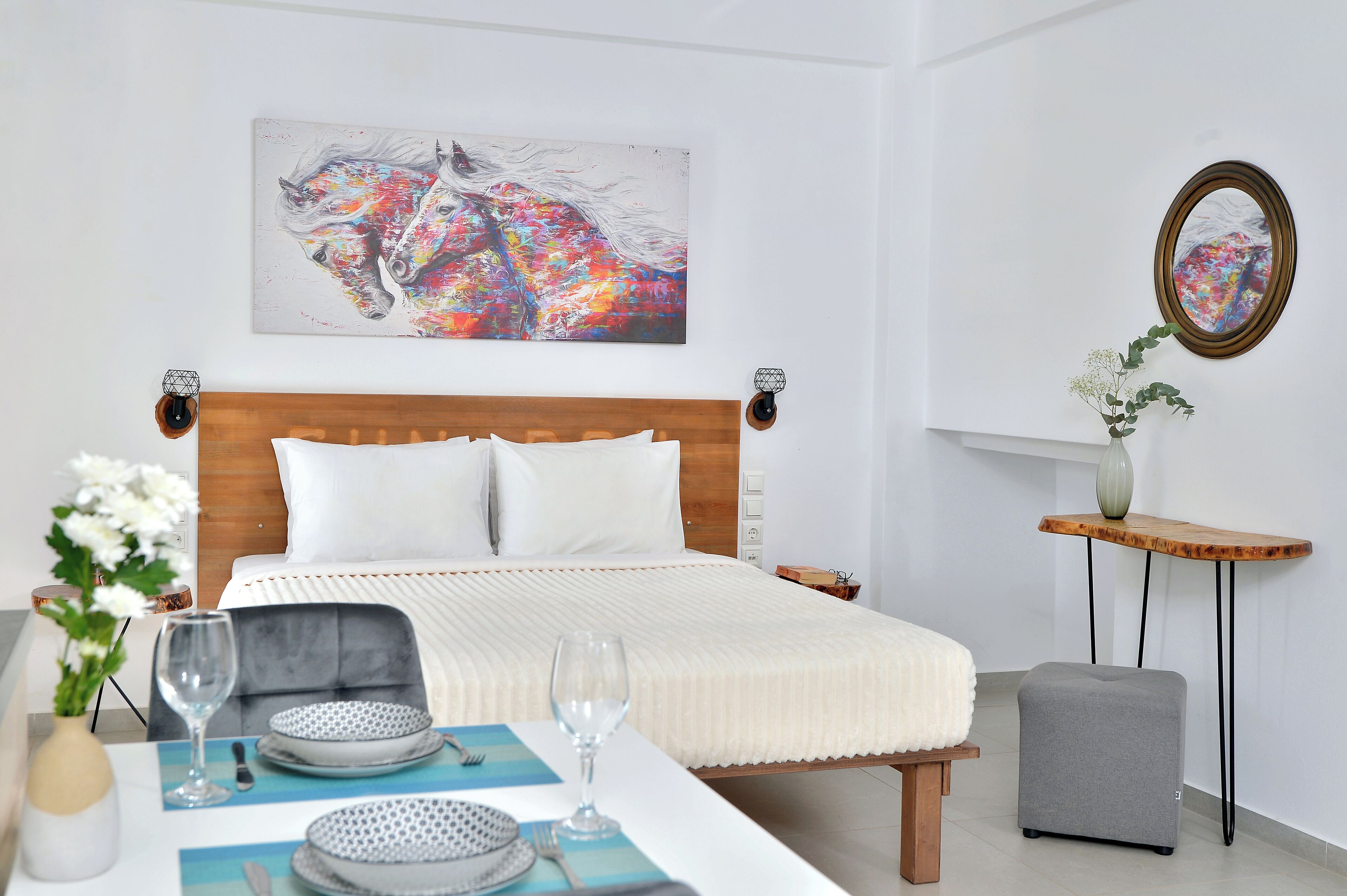 A neatly arranged bedroom with a wooden headboard, a bed with white bedding, a bedside table with a vase, and a small stool.