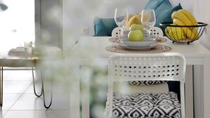 Un comedor con una mesa blanca dispuesta para dos personas, un frutero y un cesto de plátanos.