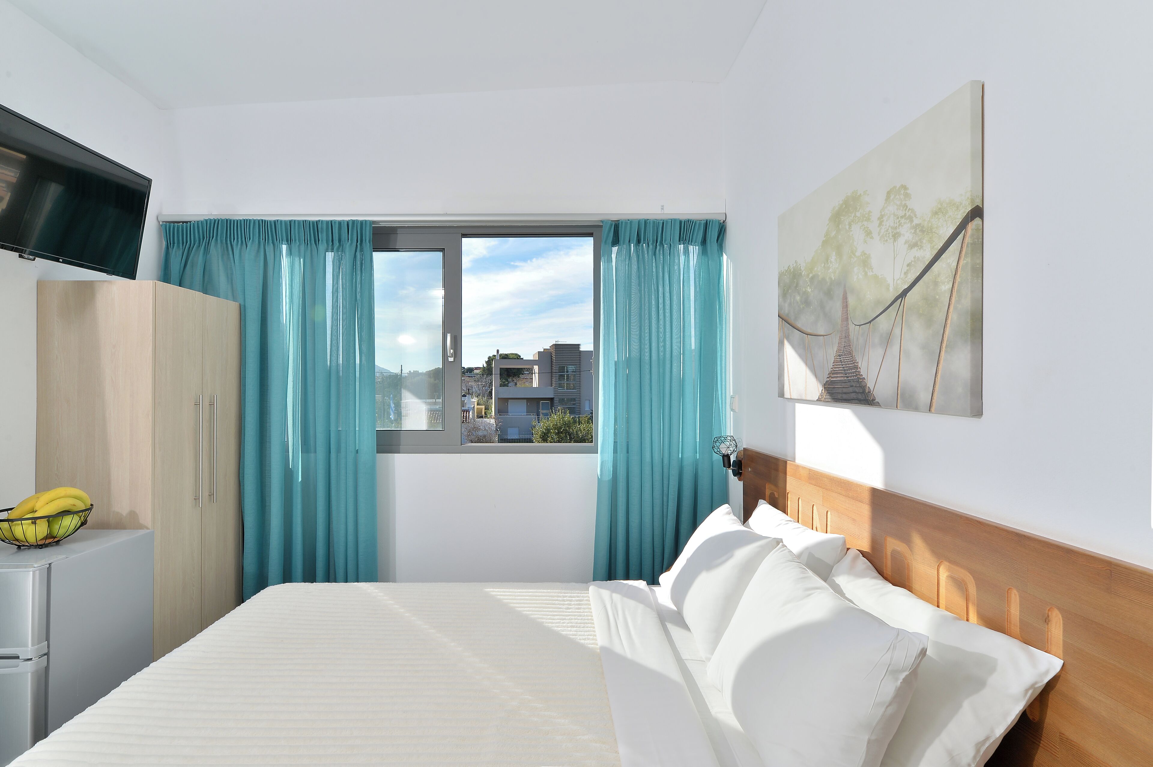 A hotel room with a bed, a television, a wardrobe, and a window with curtains.