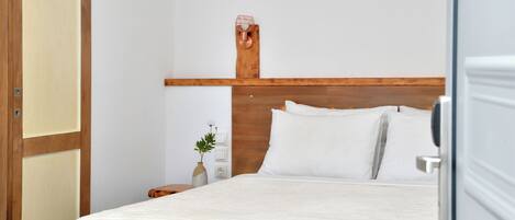 A neatly made bed with white linens in a room with wooden headboard and a simple nightstand with a vase of flowers.