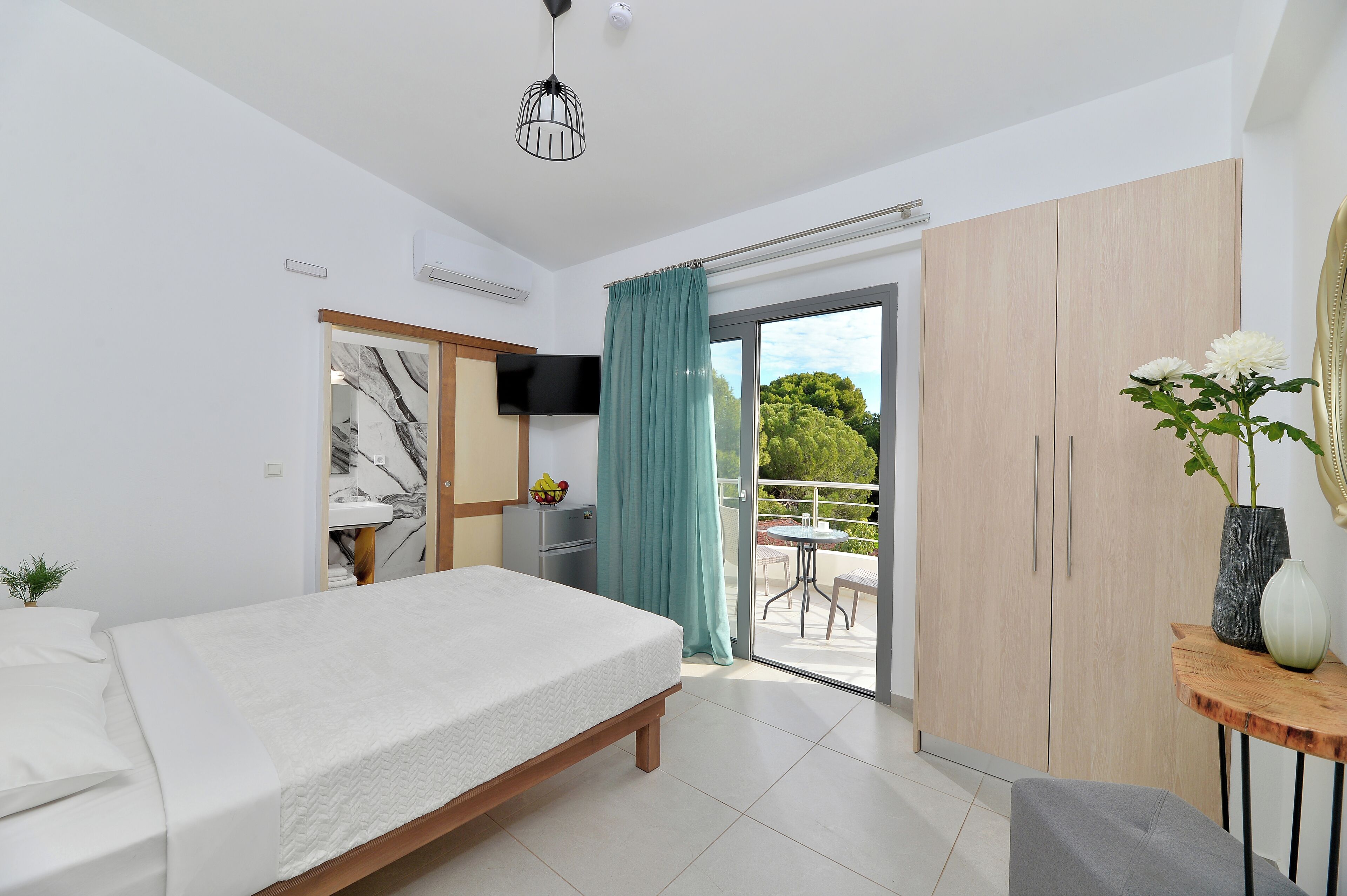 Et moderne soveværelse med seng, fjernsyn, garderobeskab og en balkon med bord og stole.