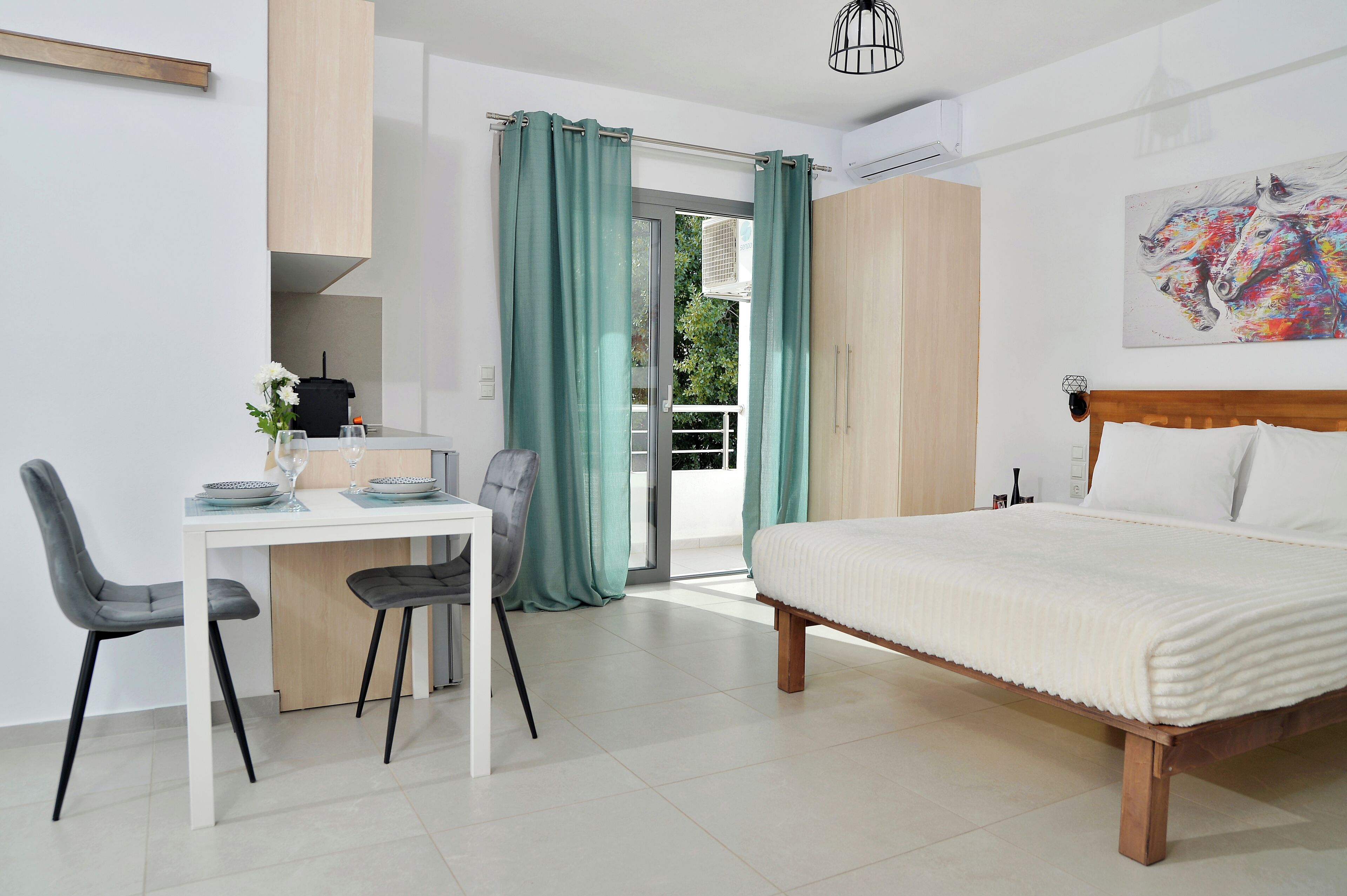 A modern bedroom with a bed, a desk with chairs, and a view through a glass door.