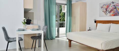 A modern bedroom with a bed, a desk with chairs, and a view through a glass door.