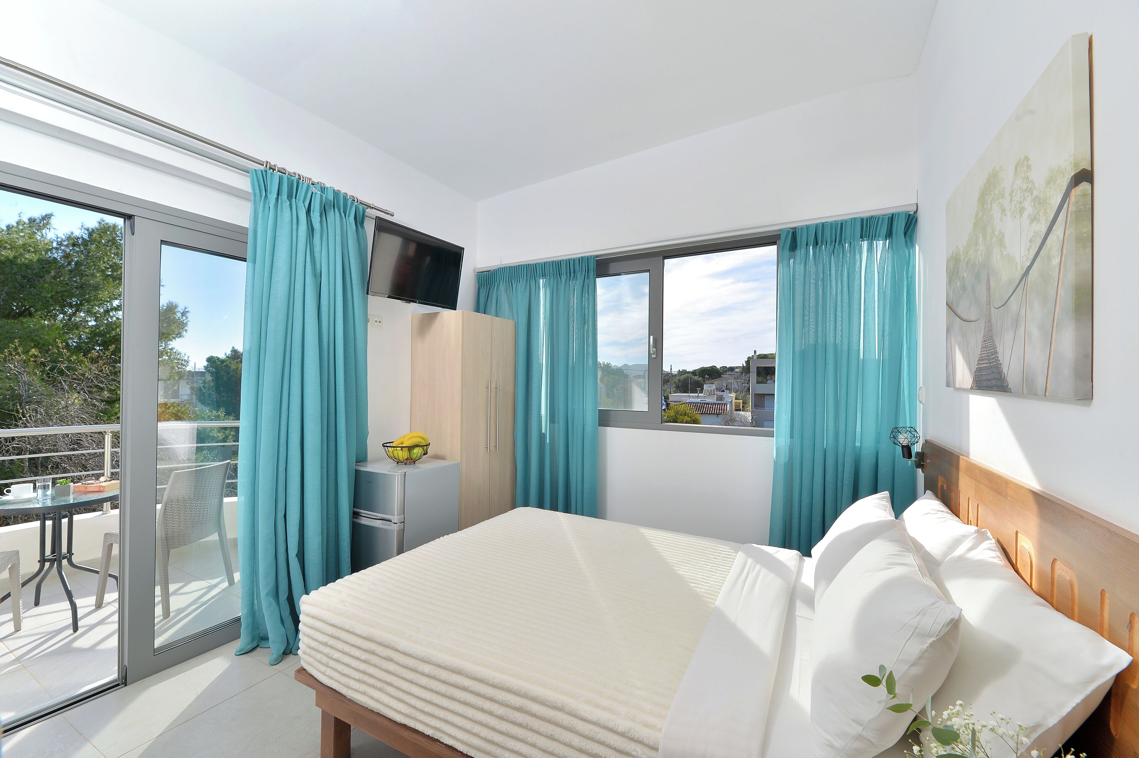 A bedroom with a bed, a TV, a desk, and a window with curtains.